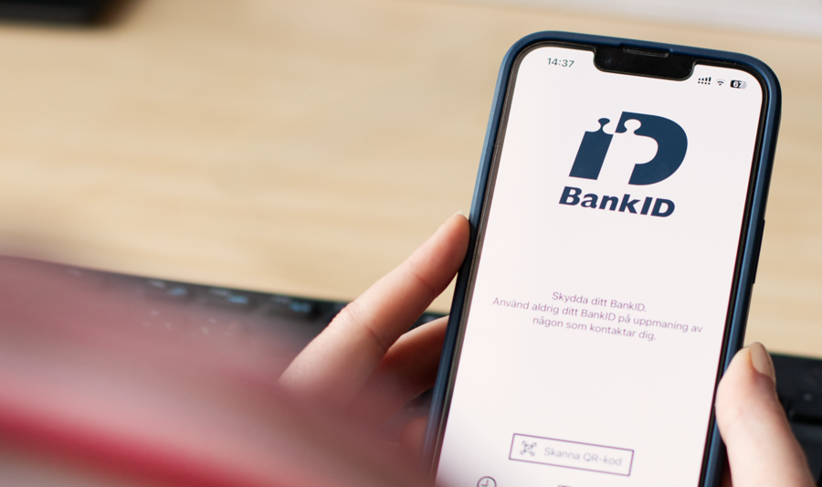 A person holding a cell phone over a desk with BankID visible on the screen.