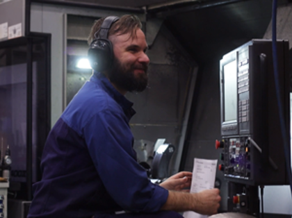 A man in a blue shirt and headphones working on a machine.