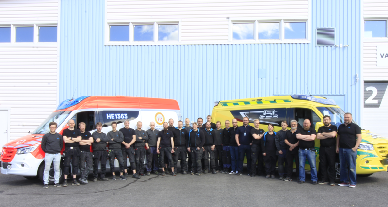 En grupp människor står framför två bilar.