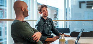 Ett par män som sitter vid ett bord med bärbara datorer.