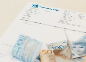 A pile of money sitting on top of an invoice from Monitor ERP.