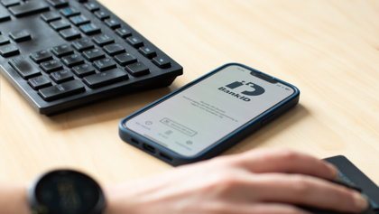 A person holding a smart phone with BankID visible on the screen, next to a keyboard.