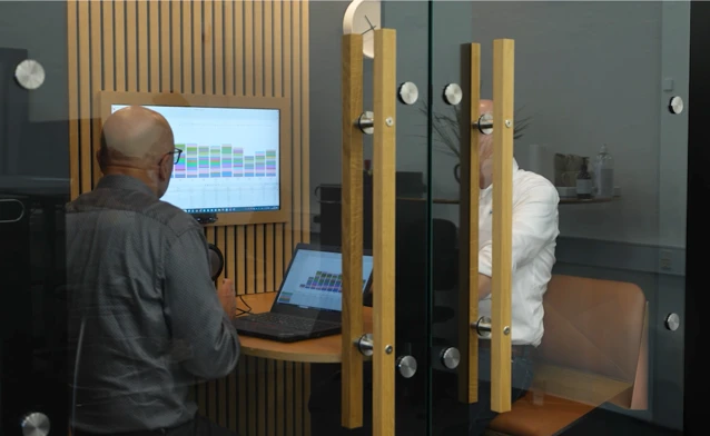 A man standing in front of a laptop computer displaying Monitor ERP dashboards. 