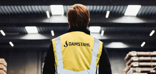 A person wearing a yellow vest with the text “Damstahl” stands inside a warehouse.