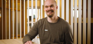 En man sitter vid ett bord och ler mot kameran.