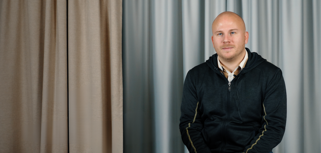 En man sitter på en stol framför en gardin.