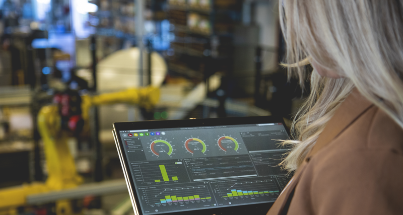 En person som håller i en surfplatta i en fabriks­miljö och visar Monitor ERP:s instrumentpanel.