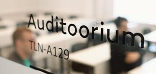 A blurry photo of a classroom at TTK University with people sitting at desks.