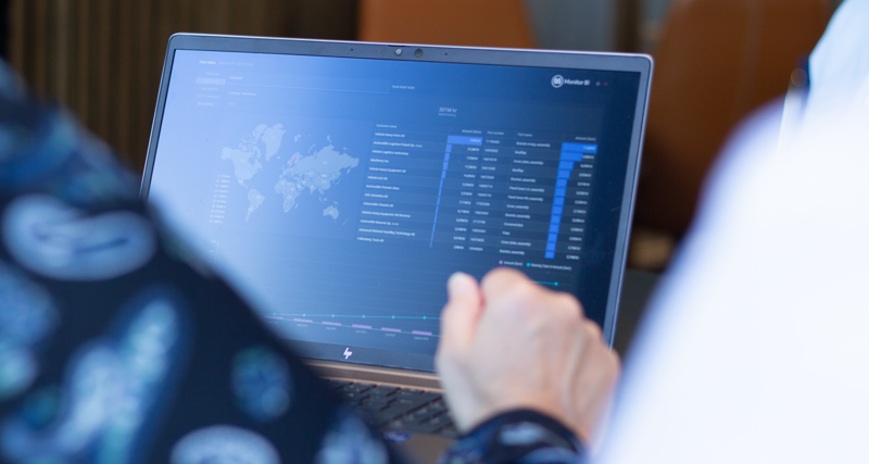 A person sitting in front of a laptop computer with Monitor BI (business intelligence) dashboards. 