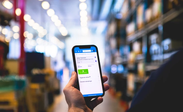 A person in a warehouse holding a cellphone displaying Monitor Mobile.