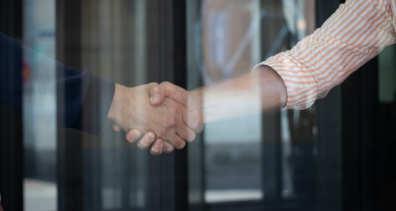 Two people shaking hands in front of a glass door.
