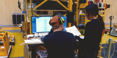 Two people standing in a manufacturing environment looking at a computer displaying a Monitor ERP dashboard.