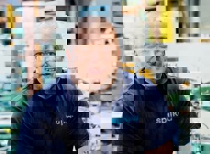 Arbeider i Spilka-fabrikken står smilende foran maskineri.