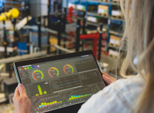 A person holding a tablet computer in a factory environment displaying Monitor ERP dashboard.