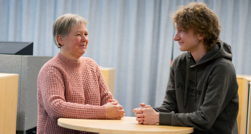 Petra Fahje and Fynn Höfer, support specialists, standing next to a table and talking to each other. 