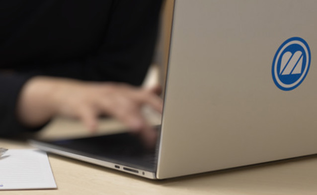A person typing on a laptop with a pen.