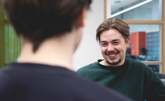 A man is smiling while talking to another man.