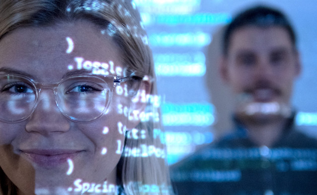 Man and a woman in front of a computer screen with code.