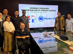Group photo of professionals from OK OCE and Monitor ERP Indonesia, standing and seated around a conference table in a modern meeting room, with a large screen displaying 'Signing Ceremony Memorandum of Understanding'