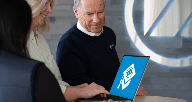 A man and a woman looking at a laptop showing Monitor Academy logo