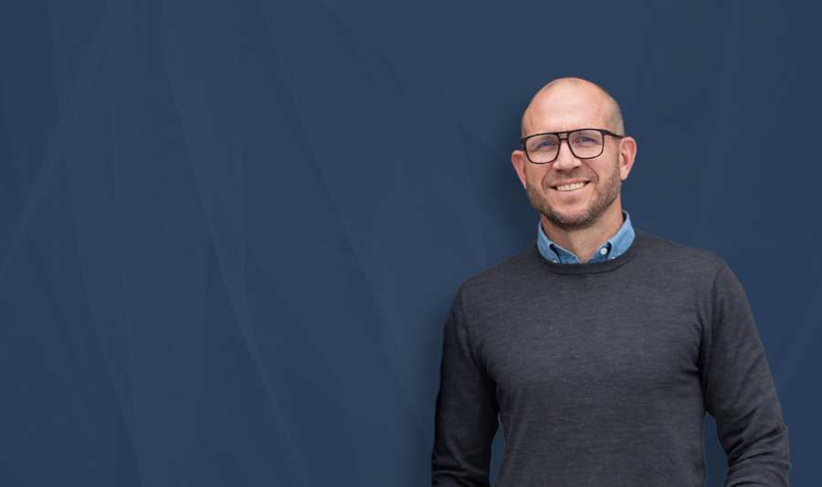 Johan Holmsten, Global säljchef på Monitor ERP, ståendes framför en blå bakgrund. 