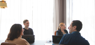A group of people sitting around a table with laptops.