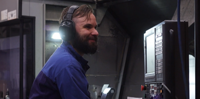 A man in a blue shirt and headphones working on a machine.