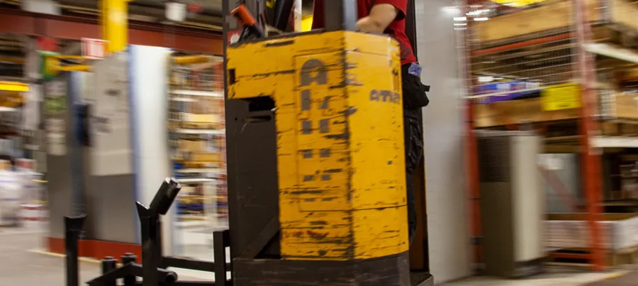 A forklift in a large warehouse with lights on.