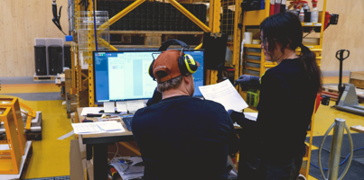 To personer står i et produktionsmiljø og kigger på en computer, der viser et Monitor ERP-dashboard.