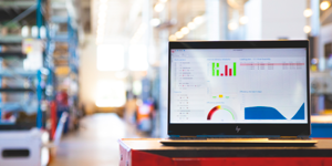 Laptop displaying charts and graphs on a screen, placed on a red table in a brightly lit industrial setting