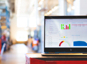 Laptop displaying charts and graphs on a screen, placed on a red table in a brightly lit industrial setting